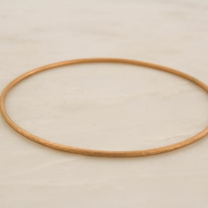 May include: A simple gold bangle bracelet. The bracelet is smooth and has a polished finish.