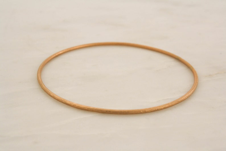 May include: A simple gold bangle bracelet. The bracelet is smooth and has a polished finish.