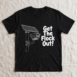 Könnte beinhalten: Ein schwarzes Kurzarm-T-Shirt mit einer weißen Linienzeichnung einer solarbetriebenen Überwachungskamera auf einem Pfosten. Rechts neben der Kamera ist der Text "Get The Flock Out!" in einer fetten, weißen, abgerundeten Schriftart gedruckt.