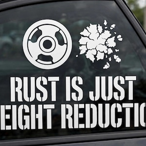 May include: A white vinyl decal applied to a car window featuring a circular weight plate icon and a jagged, cracked shape icon. Below the icons, the text reads RUST IS JUST WEIGHT REDUCTION in a bold, stencil-style font with clean, sharp edges.