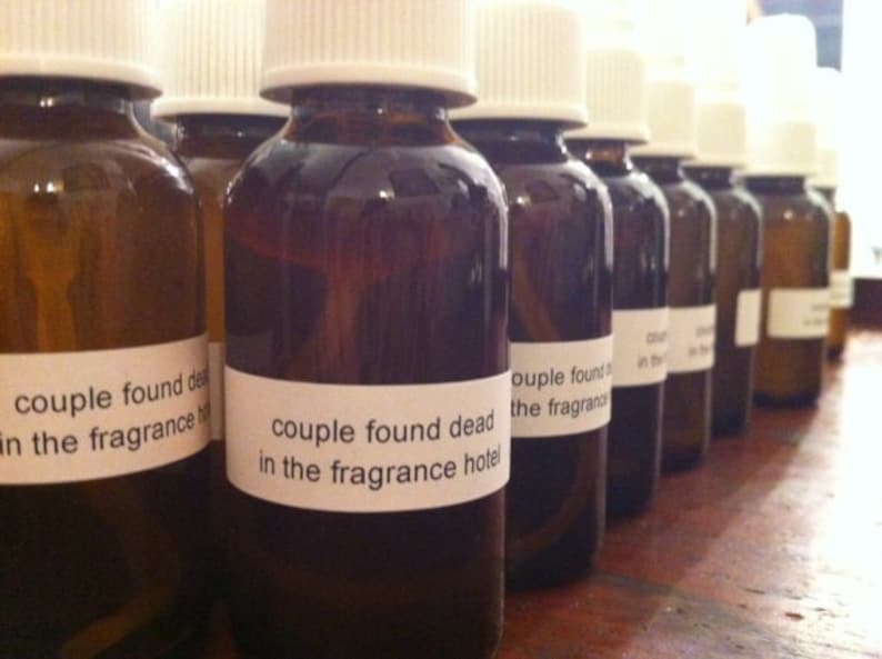 May include: A row of brown glass bottles with white caps and labels. The labels read "couple found dead in the fragrance hotel". The bottles are filled with a dark liquid.