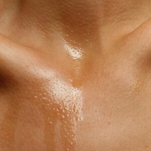 May include: Close-up of a person's chest and shoulders, with skin that appears to be glistening with moisture. The skin tone is a warm, light brown, and the moisture creates a reflective, shiny effect.