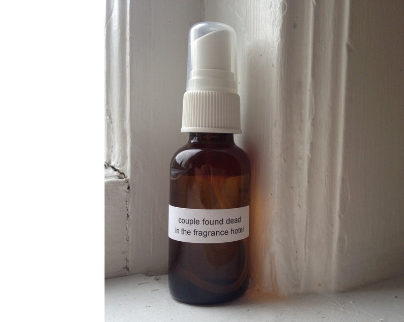 May include: A small, brown glass spray bottle with a white pump and cap. A white label on the bottle reads "couple found dead in the fragrance hotel."