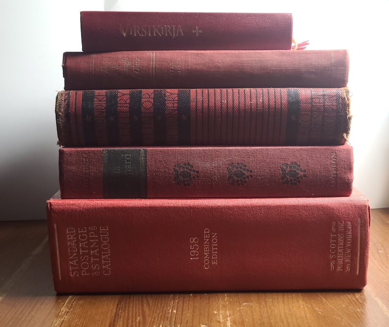 May include: A stack of six red hardcover books. The top book has the text "VIRSIKIRJA +" on the spine. The bottom book has the text "STANDARD POSTAGE STAMPS CATALOGUE 1958 COMBINED EDITION SCOTT PUBLICATIONS INC NEW YORK" on the spine.