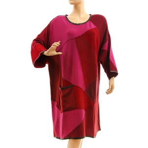 Könnte beinhalten: Ein knielanges Patchwork-Kleid in Rot- und Rosatönen. Es hat einen runden Ausschnitt, lange Ärmel und zwei Vordertaschen. Das Kleid hat schwarze Paspeln an Ausschnitt, Manschetten und Taschen. Das Kleid hat eine lockere Passform.