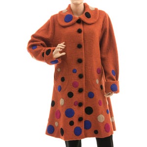 Può includere: Un lungo cappotto di lana marrone con colletto a pettorina e chiusura con bottoni. Il cappotto è decorato con cerchi di feltro colorati di varie dimensioni.
