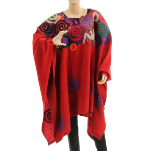 Op de afbeelding: Een rode poncho met een bloemenontwerp. De poncho heeft een levendig patroon van kleurrijke rozen en krullen op de schouders en mouwen. De hoofdband van de poncho is effen rood, met spleten aan de zijkanten voor de armen.