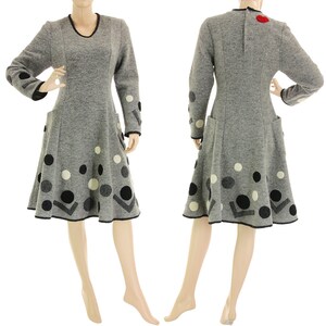 Könnte beinhalten: Ein graues Kleid mit langen Ärmeln und ausgestelltem Rock. Das Kleid hat schwarze, weiße und graue Polka Dots und geometrische Formen. Der Ausschnitt und die Manschetten sind schwarz eingefasst. Auf dem Rücken befindet sich eine rote Applikation.