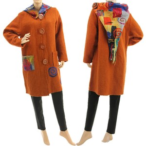 Könnte beinhalten: Ein orangefarbener Wollmantel mit einer bunten, gemusterten Kapuze und Akzenten. Der Mantel hat große Holzknöpfe, Taschen und dekorative Aufnäher. Der Mantel ist knielang und wird mit einer schwarzen Hose getragen.