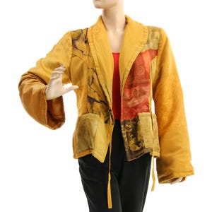 May include: Mustard yellow jacket with patchwork design. The jacket features a shawl collar, long sleeves, and two front pockets. The fabric has a textured appearance with floral and abstract patterns in shades of red, brown, and black.