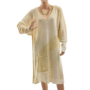 Könnte beinhalten: Ein cremefarbenes, langärmliges Kleid mit V-Ausschnitt und lockerer Passform. Das Kleid hat ein Patchwork-Design mit verschiedenen Cremetönen und eine einzelne Tasche. Eine goldfarbene Halskette wird mit dem Kleid getragen.