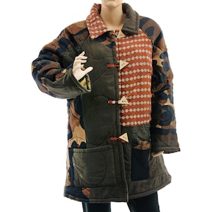 Könnte beinhalten: Eine Patchwork-Steppjacke mit einzigartigem Design. Die Jacke hat eine Mischung aus Tarn-, Braun- und Rostfarbenen Stoffen. Sie hat dreieckige Holzverschlüsse und einen Kragen. Die Jacke wird auf einer Schaufensterpuppe präsentiert.