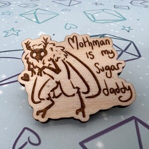 May include: A wooden cutout of a mothman with the text "Mothman is my Sugar Daddy" written below it.