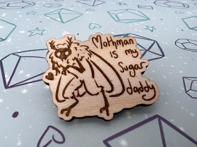 May include: A wooden cutout of a mothman with the text "Mothman is my Sugar Daddy" written below it.