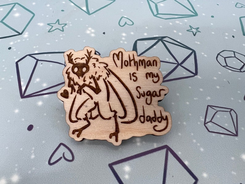 May include: A wooden cutout of a mothman with the text "Mothman is my Sugar Daddy" written on it.