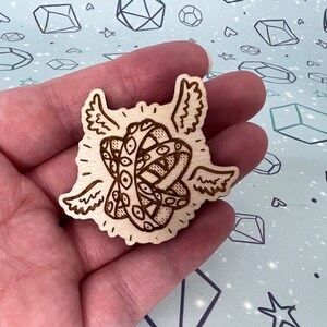 May include: A wooden cutout of a pair of eyes with wings, resembling a mythical creature. The eyes are detailed with intricate patterns and the wings are spread out.