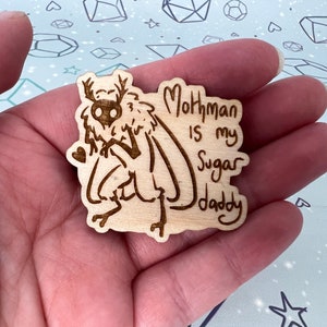 May include: A wooden cutout of a mothman with the text "Mothman is my Sugar Daddy" on a light brown background.