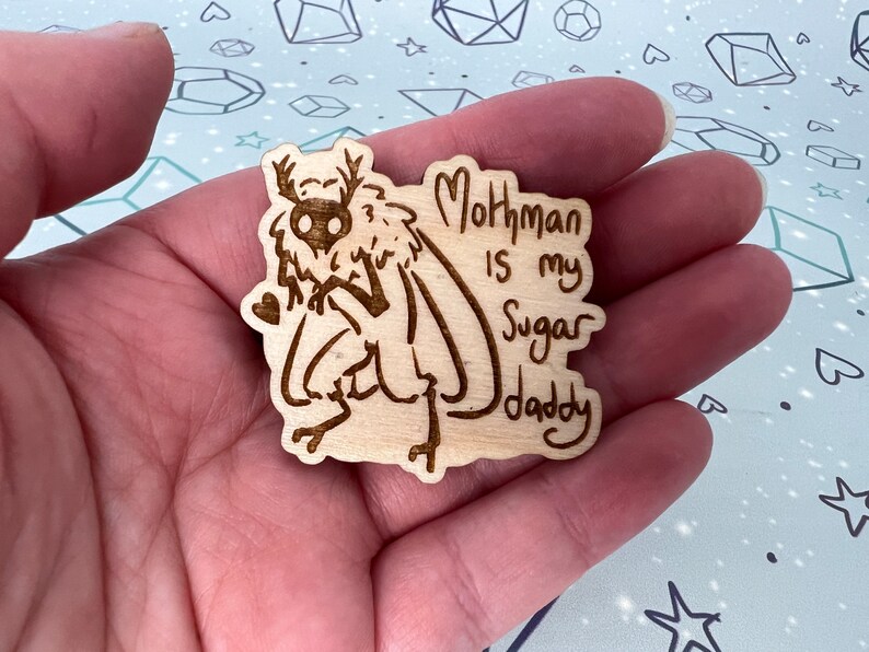 May include: A wooden cutout of a mothman with the text "Mothman is my Sugar Daddy" on a light brown background.