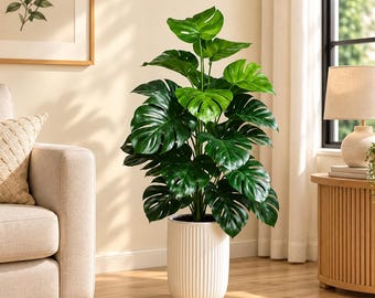 May include: A tall artificial monstera plant with large, glossy, dark green split leaves. The plant is housed in a cylindrical white planter featuring a vertical ribbed texture on the exterior, standing upright on a wooden floor surface.