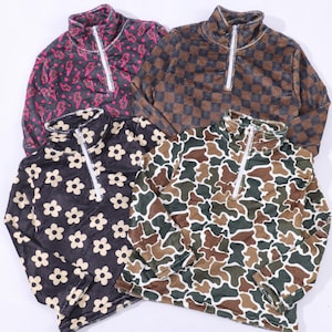 May include: Four long-sleeve quarter-zip pullovers featuring distinct patterns: a black and pink lightning bolt print, a brown and black checkerboard, a black and white flower print, and a green, brown, and white camouflage pattern.
