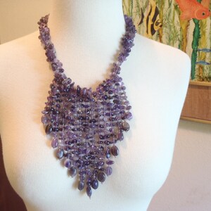 May include: A multi-strand bib necklace featuring numerous small, polished purple amethyst gemstone chips arranged in a cascading, web-like pattern that tapers to a point at the center, secured by a matching amethyst chip collar.