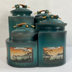 May include: Set of four teal ceramic canisters with bamboo lids and painted scenes of palm trees and a sunset. The canisters are arranged in a staggered stack.