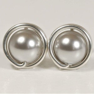 May include: A pair of silver earrings with a pearl in the center of each earring. The pearl is surrounded by a silver wire circle.