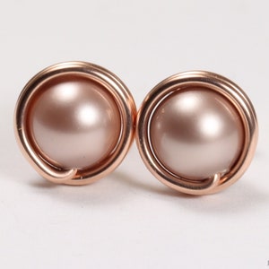 May include: A pair of rose gold earrings with a single blush pink pearl in each earring. The pearl is set in a rose gold wire circle.