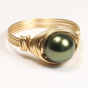 May include: A gold wire wrapped ring with a dark green pearl. The ring is made with multiple strands of gold wire that are twisted together to create a unique and delicate design.