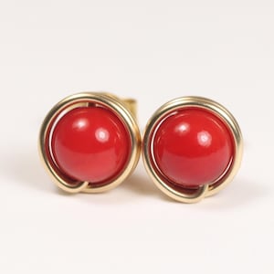 May include: A pair of gold stud earrings with red coral gemstones. The earrings have a simple, elegant design.