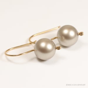 May include: A pair of gold hoop earrings with a large, round, pearl-like drop in a light gray color.