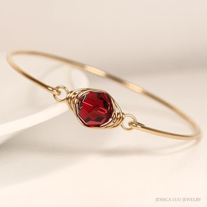 May include: A gold wire wrapped bracelet with a single red gemstone.