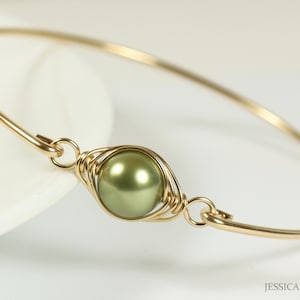 Puede incluir: Un brazalete de oro con una sola perla verde envuelta en alambre dorado.