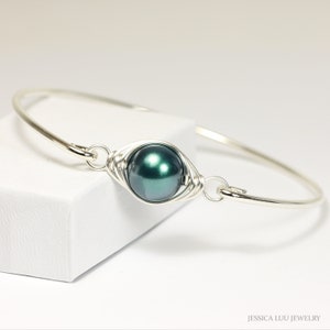 May include: A silver bangle bracelet with a dark green pearl wrapped in silver wire.