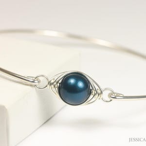 Puede incluir: Un brazalete de plata con una perla azul oscuro envuelta en alambre plateado.
