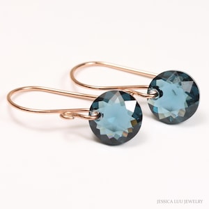 May include: A pair of rose gold dangle earrings with blue crystal stones. The earrings have a simple design and are perfect for everyday wear.
