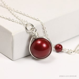 May include: A silver chain necklace with a red pearl pendant. The pearl is wrapped in silver wire and hangs from a silver chain.