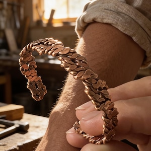 May include: A copper cuff bracelet featuring a thick, braided, chain-link design with a textured, metallic finish. The bracelet is open-ended, allowing for adjustment, and displays a warm, reddish-brown hue characteristic of polished copper metal.