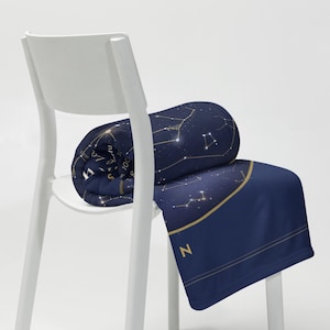 Printful mockup of the star map throw blanket rolled on a white chair.