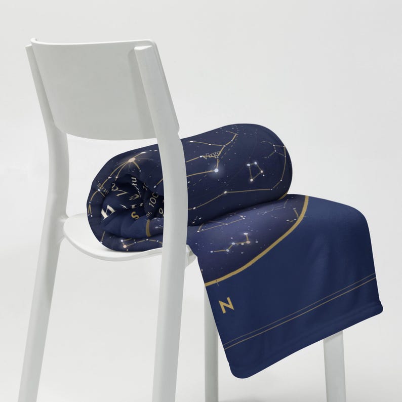 Printful mockup of the star map throw blanket rolled on a white chair.