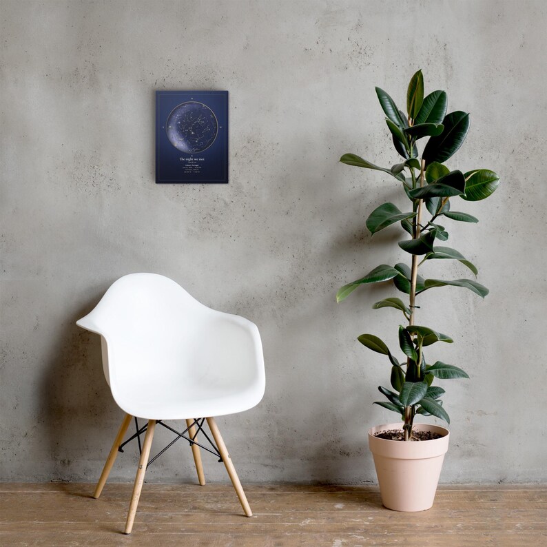 Mockup of a personalized star map canvas on a grey wall beside a chair and plant. Props are not included.