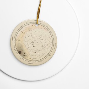 The round ceramic star map ornament with its gold cord on a white plate, Printful mockup.