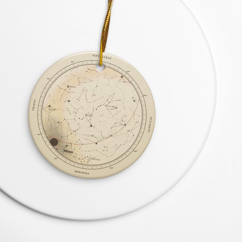 The round ceramic star map ornament with its gold cord on a white plate, Printful mockup.