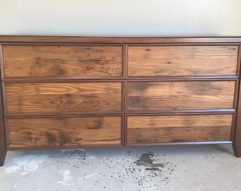 May include: A six-drawer dresser made of reclaimed wood with a dark brown stain. The dresser has a simple design with a rectangular top and straight legs.