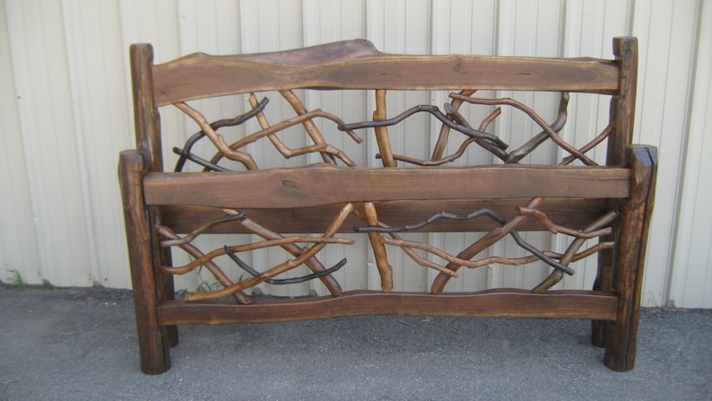 May include: A rustic wooden headboard with a unique design featuring interwoven branches. The headboard is stained a dark brown colour and has a natural, organic look.