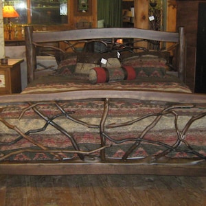 May include: A rustic wooden bed frame with a headboard and footboard made of branches. The bed is covered with a brown and red patterned blanket and has a few pillows on top.