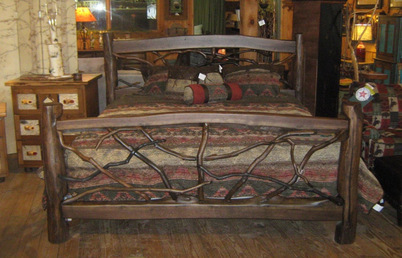 May include: A rustic wooden bed frame with a headboard and footboard made of branches. The bed is covered with a brown and red patterned blanket and has a few pillows on top.