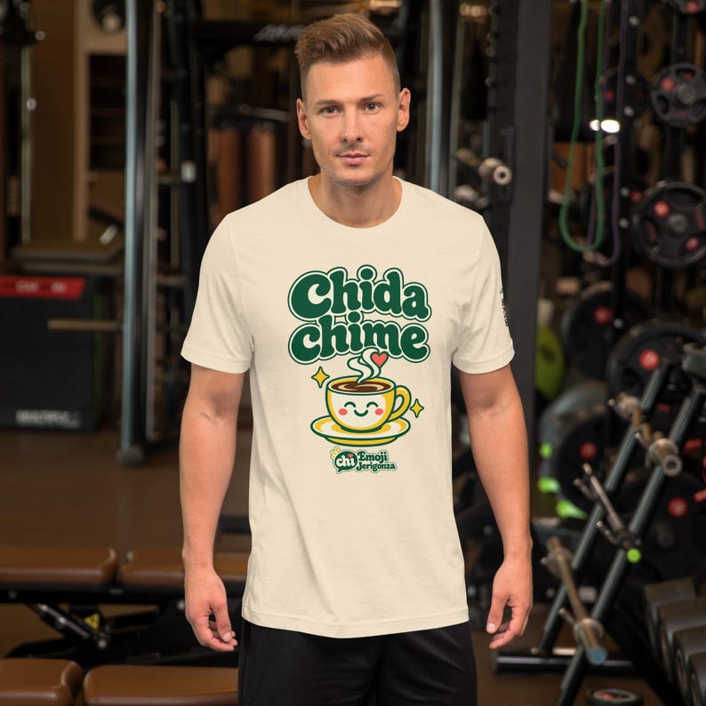 Man in a gym wearing the Heather Natural t-shirt with the Chida chime design: green bubble letters, a smiling coffee cup on a saucer and gold sparkles.