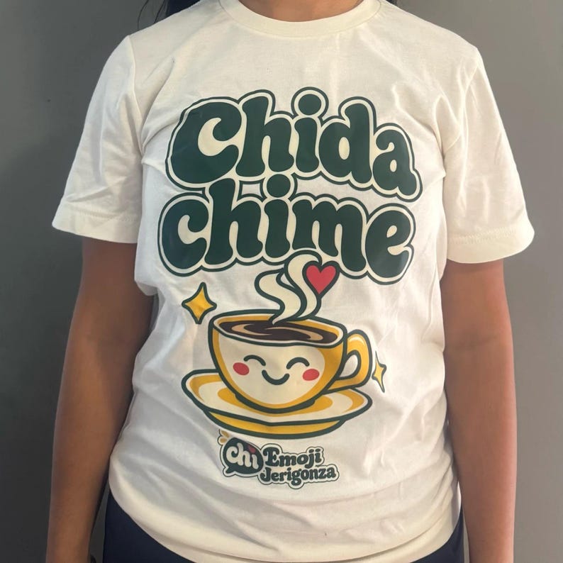Real photo of the Heather Natural Chida chime t-shirt worn, showing the green retro letters, smiling coffee cup with a coral heart, and the Emoji Jerigonza logo.