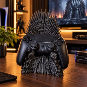 May include: A black video game controller resting on a dark gray stand shaped like a throne made of numerous pointed swords. The controller features standard directional buttons, two analog sticks, and action buttons, all in a matte black finish.